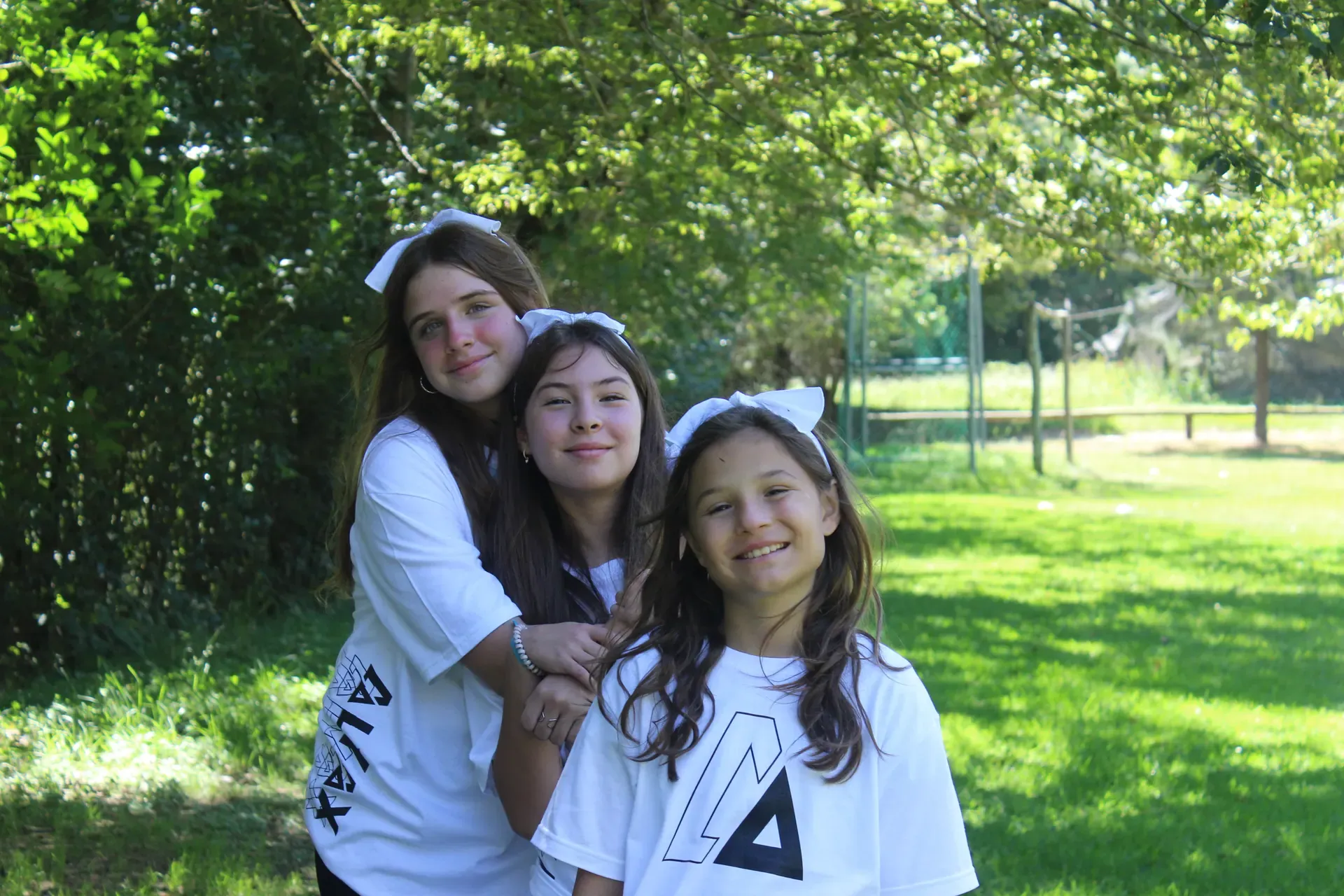 Tres niñas con playeras blancas de ALYAX abrazadas en el jardín
