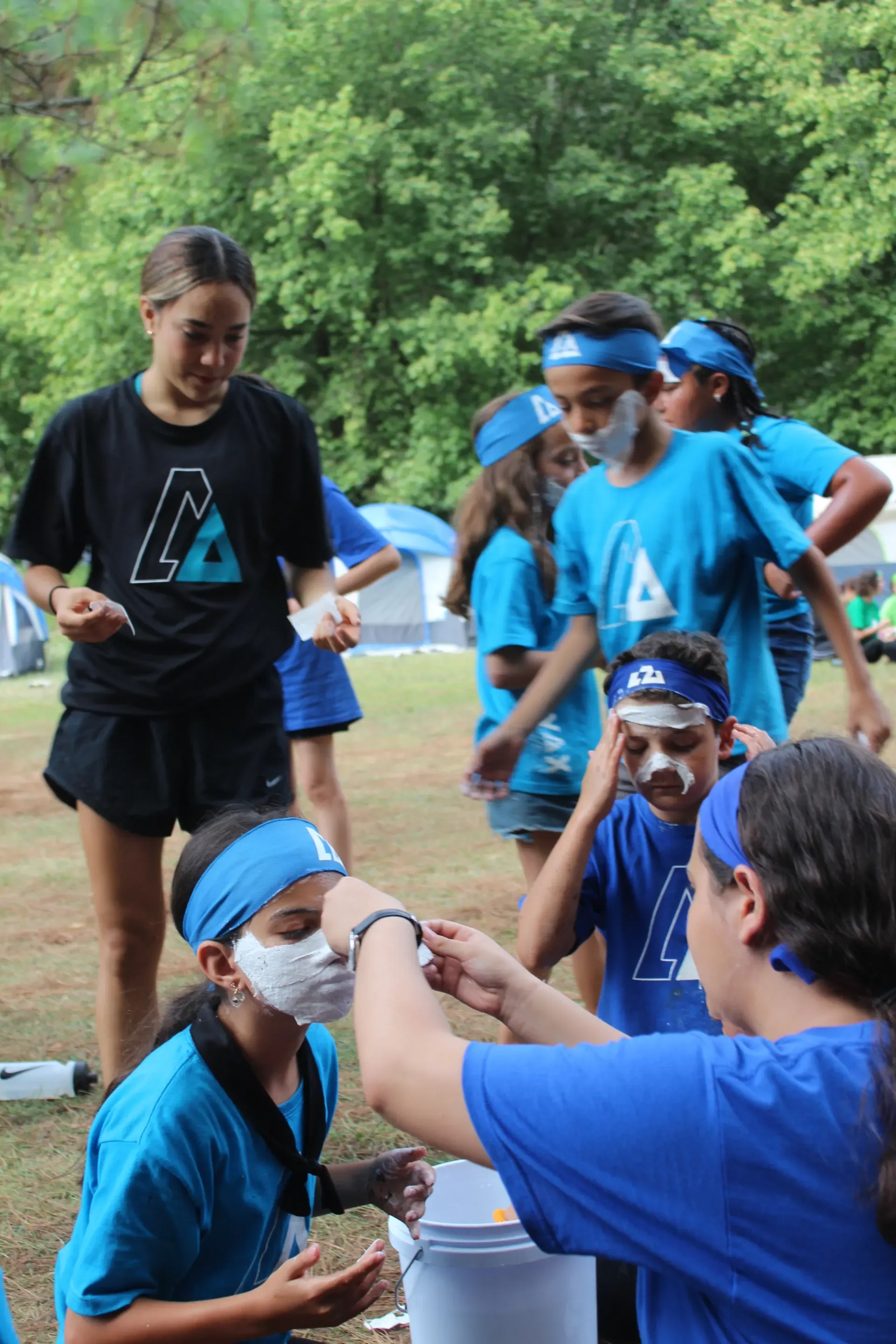 Campistas con playeras azules pintándose la cara entre ellos antes de una actividad