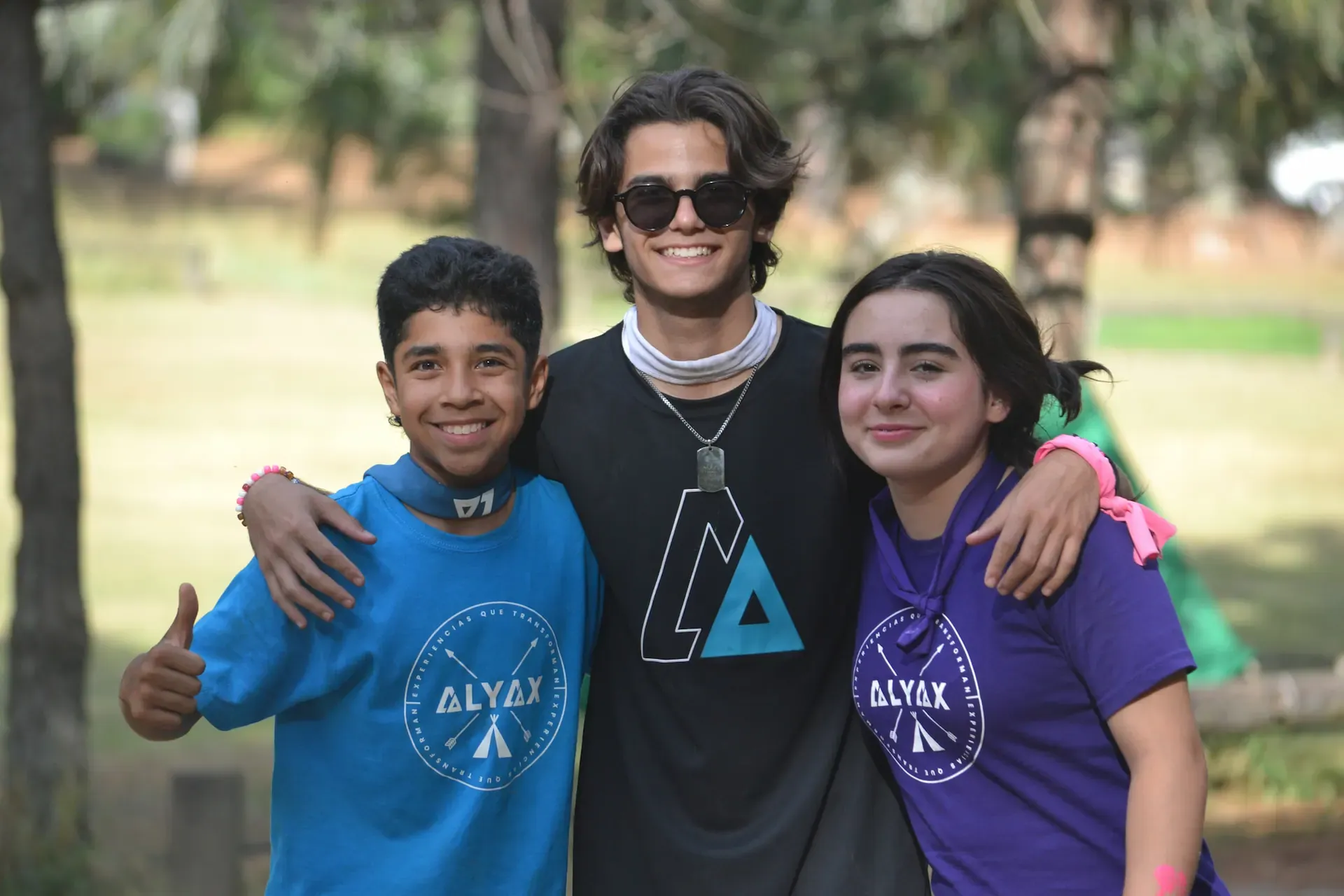 Tres campistas abrazados sonriendo a la cámara en el jardín
