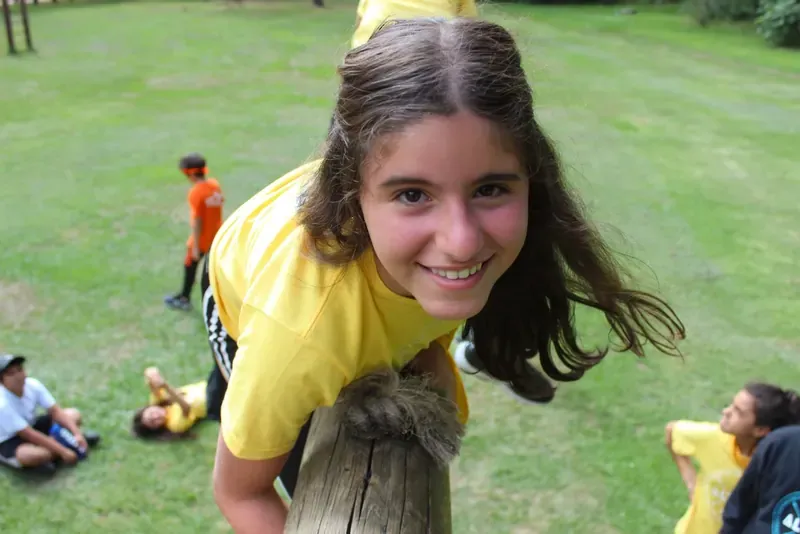 Niña con playera amarilla sonriendo recargada en un tronco
