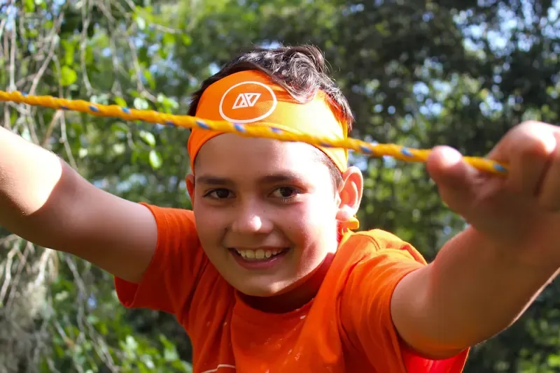 Niña con playera naranja y banda en la cabeza sonriendo junto a una cuerda