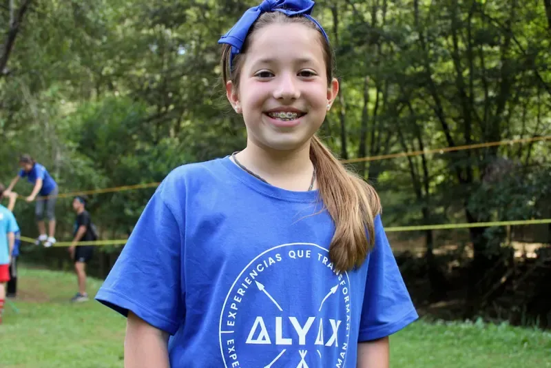 Niña con playera azul de ALYAX sonriendo a la cámara