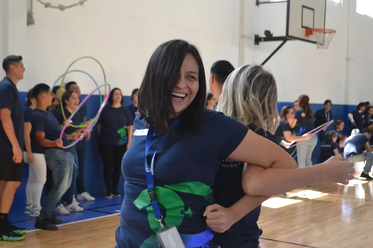 Maestra sonriente con un listón verde participando en una dinámica de integración en el gimnasio del colegio