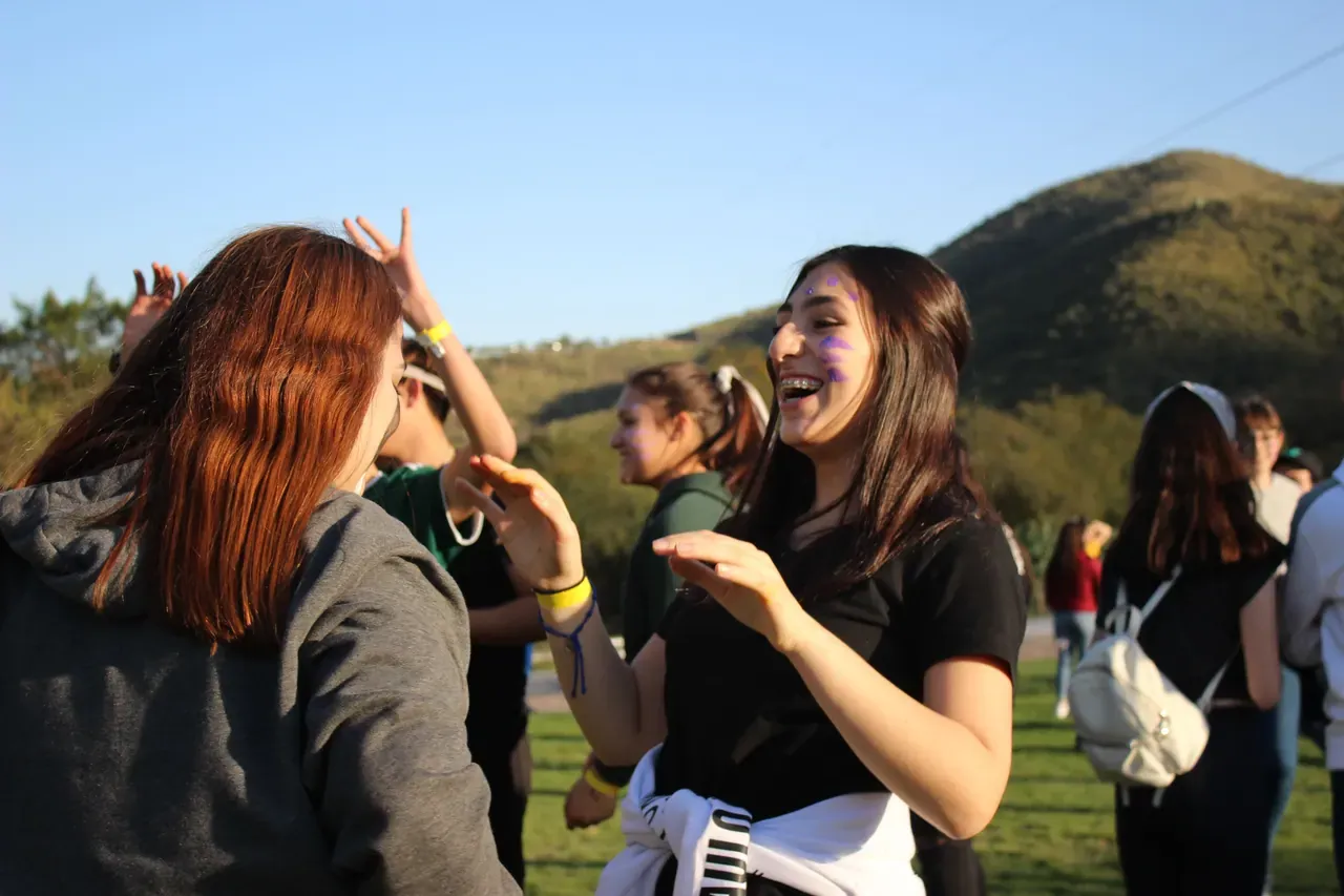 Dos compañeras riendo juntas durante una actividad al aire libre, mostrando el impacto positivo de la integración