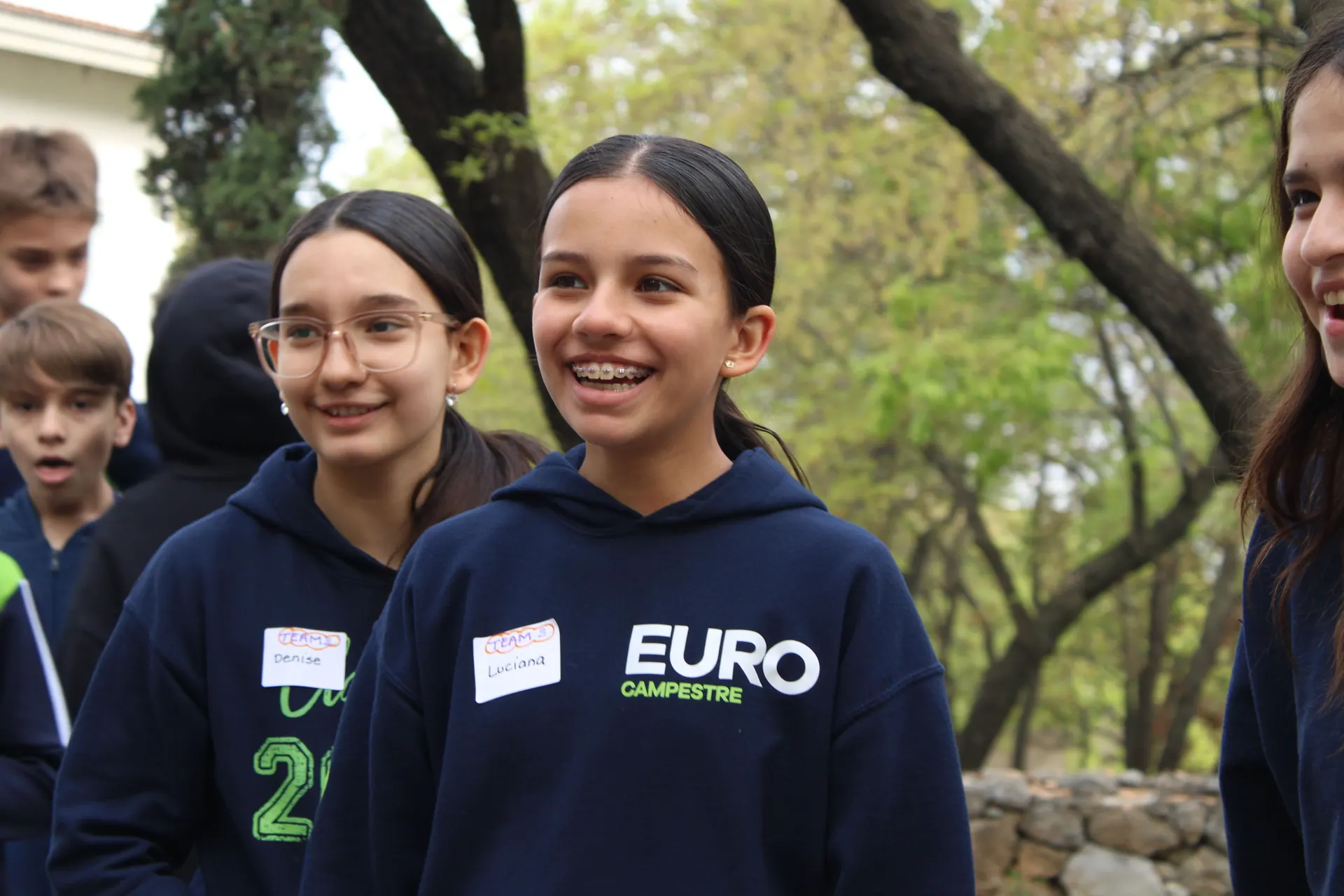 Joven sonriendo mientras interactúa con otros estudiantes, mostrando un ambiente de confianza y diversión