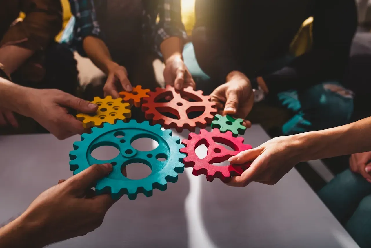 Manos de un equipo uniendo engranes de colores, símbolo de la coordinación que se logra con un buen liderazgo