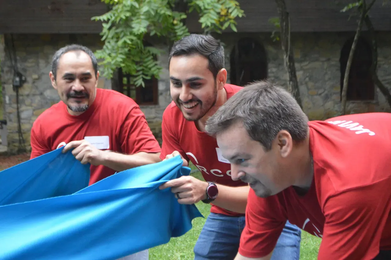 Colaboradores con playeras rojas sosteniendo una lona azul durante un rally empresarial
