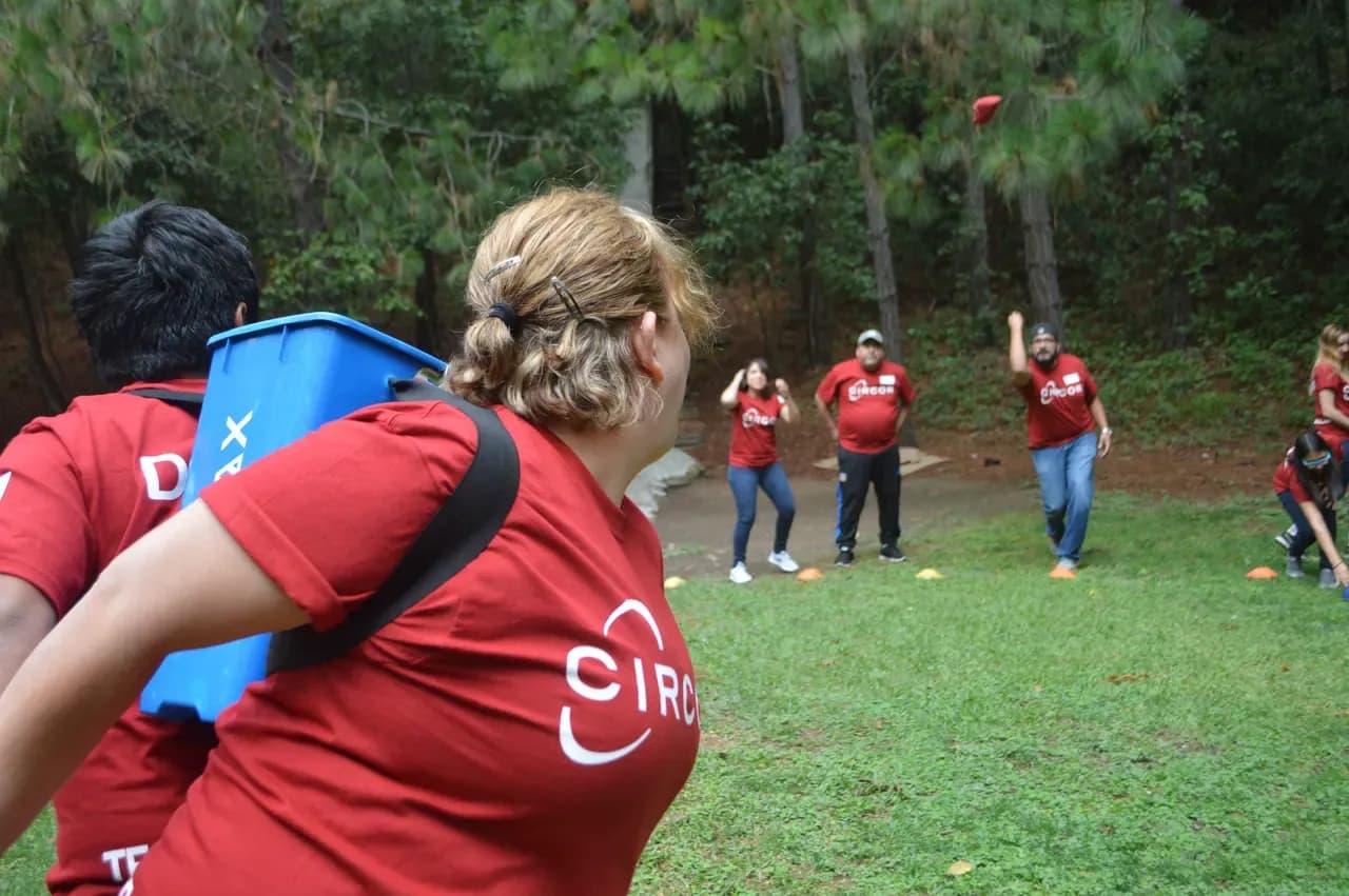 Colaboradora con un contenedor a la espalda lista para atrapar lo que lanzan sus compañeros en un juego de equipo al aire libre